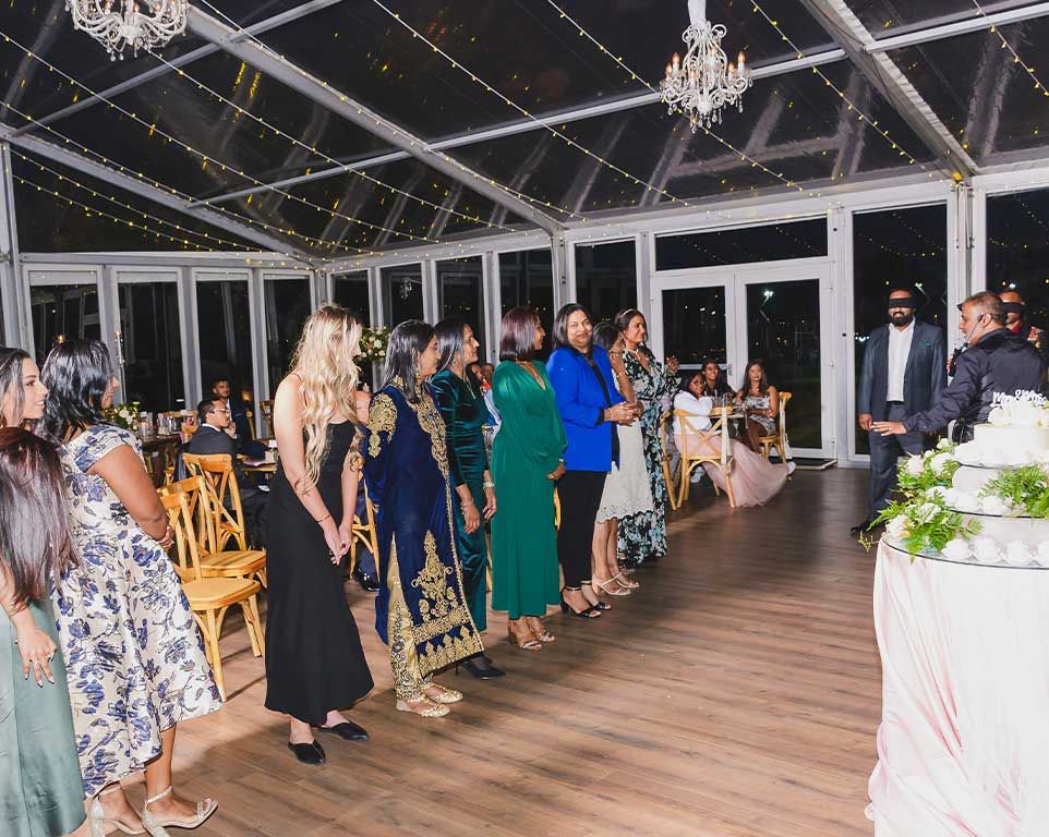 Wedding guests lined up for a reception game under fairy-light chandeliers
